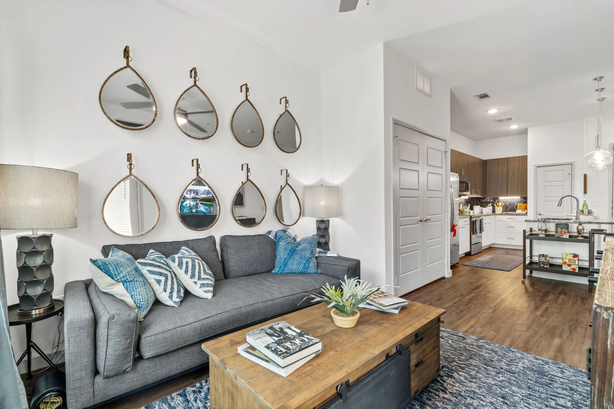 A cozy living room featuring a grey sofa, wooden coffee table, and decorative teardrop mirrors on the wall.